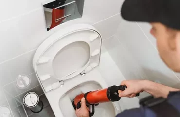 Plumber unclogging toilet with professional force pump cleaner_
